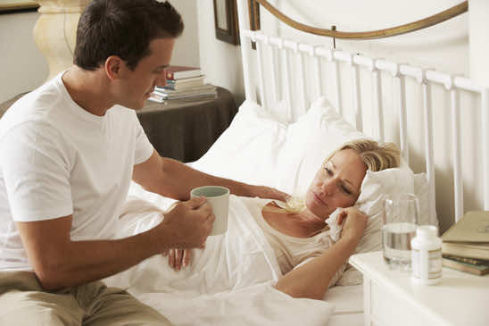Husband Bringing Sick Wife Hot Drink In Bed At Home